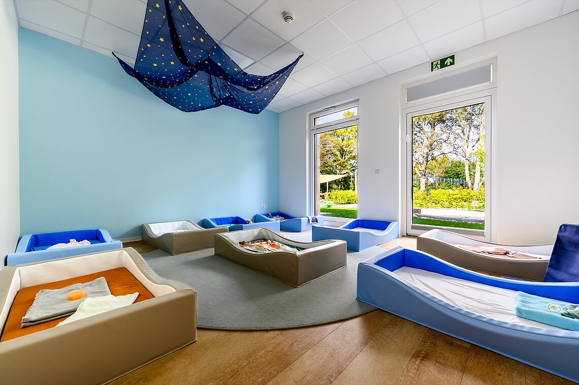 Ein Kinderzimmer mit mehreren Betten und einem blauen Baldachin, gestaltet nach dem frühkindlichen Bildung- und AWO-Kitas pädagogischen Konzept.