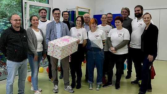 Eine Gruppe von Menschen posiert für ein Foto und hält ein Geschenk in der Hand.