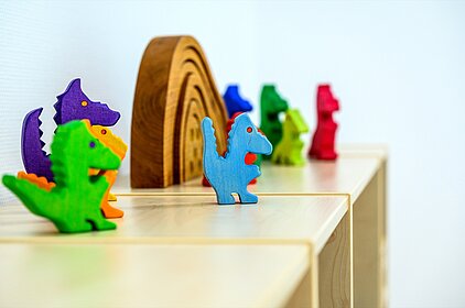 Bunte Holzdinosaurier auf einem Regal im Kinderzimmer fördern frühkindliche Bildung.