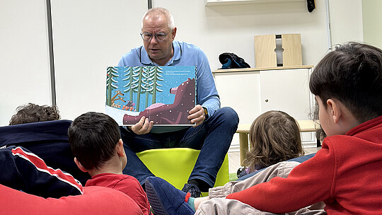 Ein Mann liest Kindern in einem Klassenzimmer ein Buch vor.