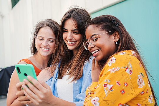 Drei junge Frauen nutzen ein Mobiltelefon für die mobile soziale Jugendarbeit de AWO in Mönchengladbach.